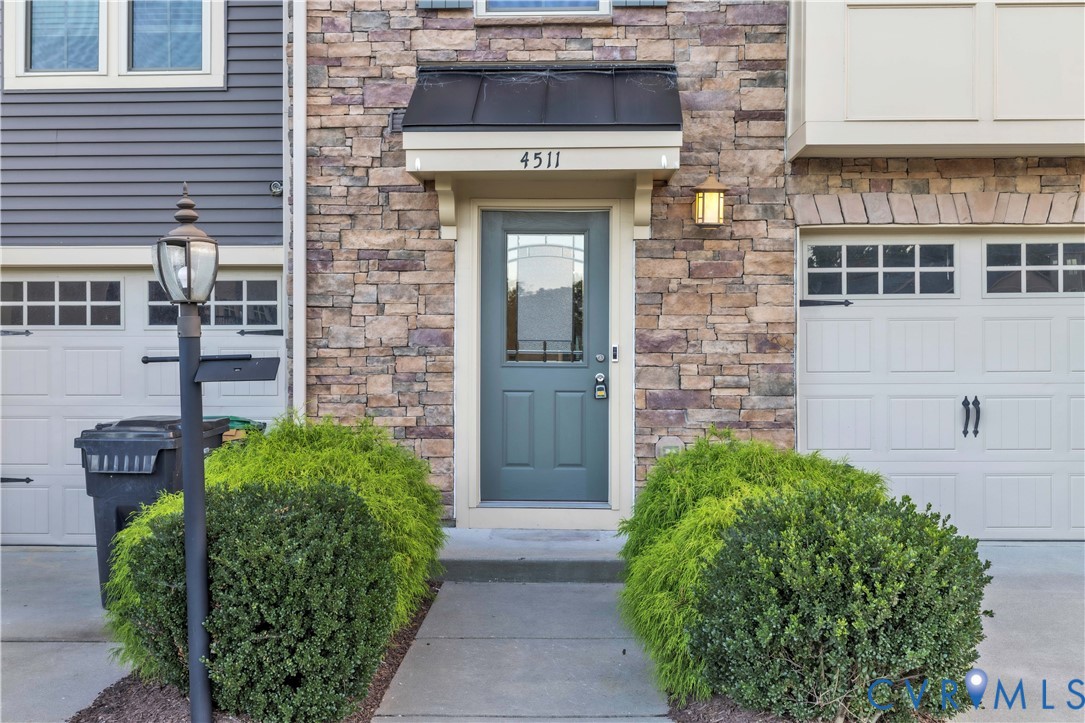 Exterior facade featuring multi-tonal masonry veneer, a dark metal door awning, a paneled entry door with an arched glass insert, and two carriage-style garage doors Exterior facade featuring multi-tonal masonry veneer, a dark metal door awning, a paneled entry door with an arched glass insert, and two carriage-style garage doors