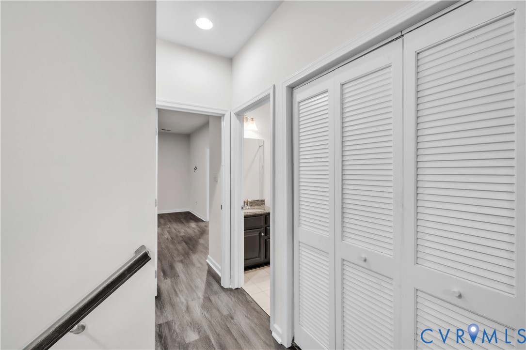 Hallway featuring louvered closet doors, wood-finish flooring, and recessed ceiling lighting