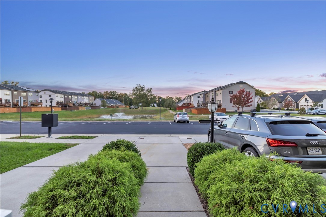 Concrete driveway leading to paved parking area featuring landscaped shrubbery, a central water fountain, and exterior lighting fixtures Concrete driveway leading to paved parking area featuring landscaped shrubbery, a central water fountain, and exterior lighting fixtures