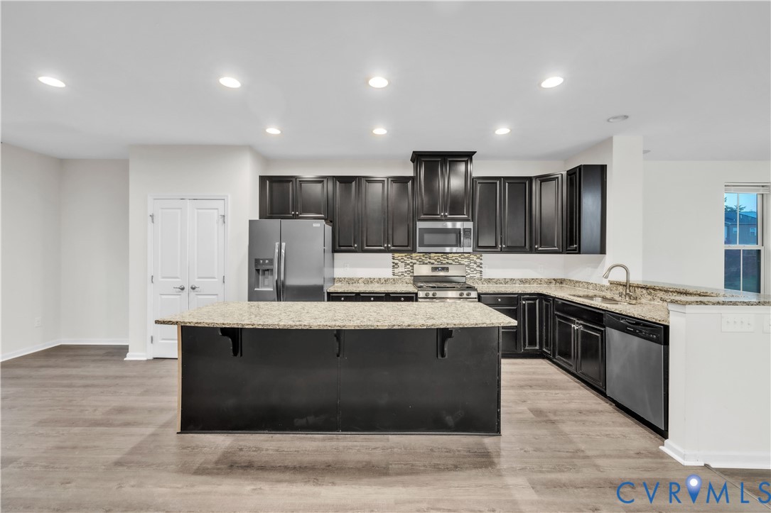 Kitchen featuring dark-finish cabinetry, stone-surface countertops, center island, recessed lighting, and wood-finish flooring