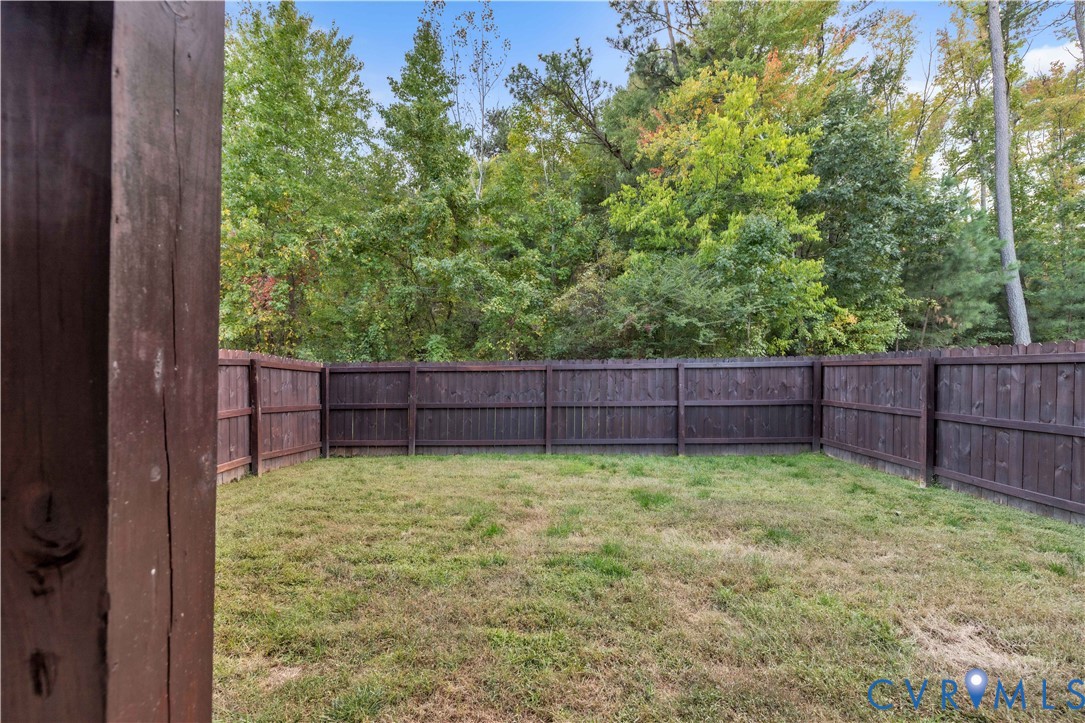 Backyard featuring a wood-panel privacy fence and a natural grass lawn, bordered by mature trees