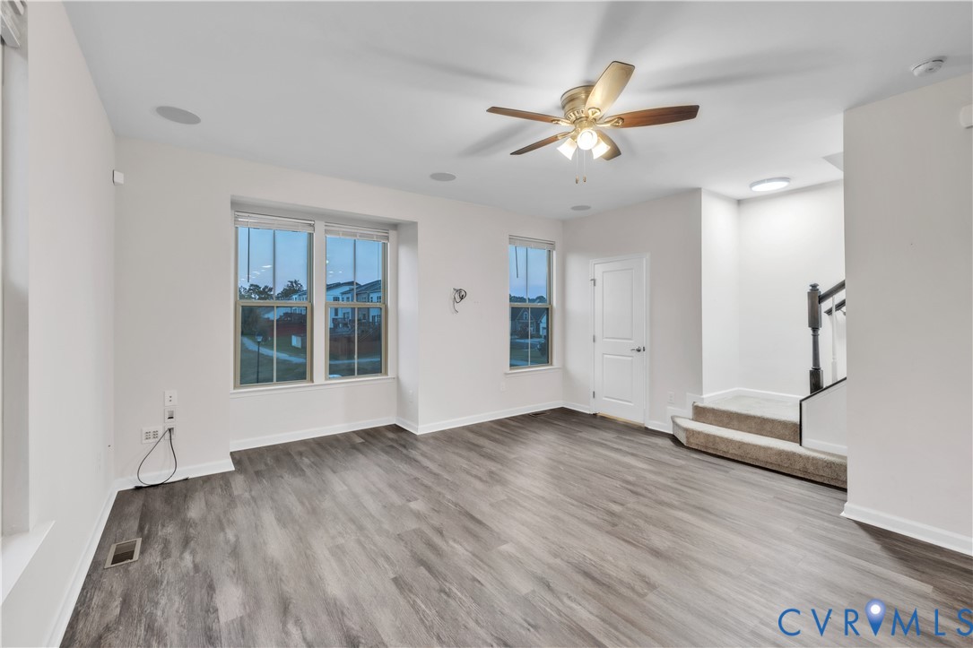 Interior area featuring wood-finish flooring, recessed lighting, a multi-blade ceiling fan with integrated light fixture, windows with multi-pane glass, and carpeted stairs with a decorative spindle railing