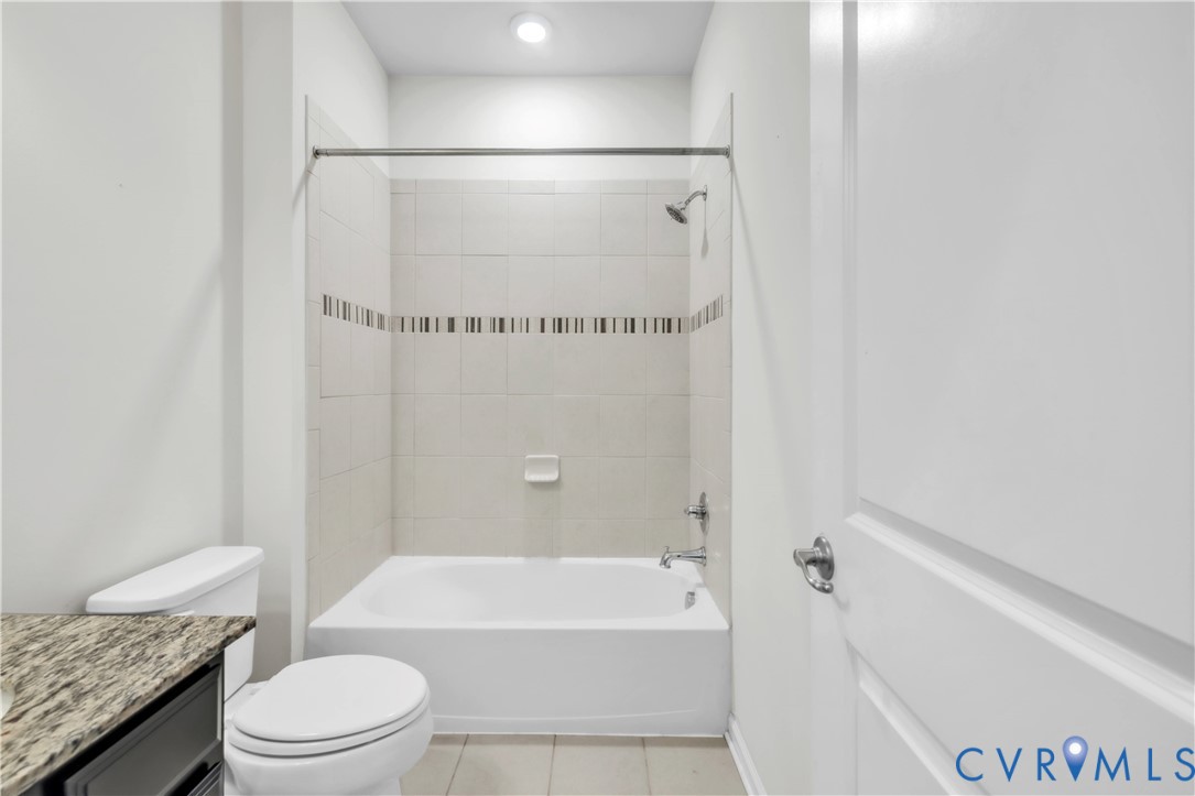Bathroom featuring a tub and shower combination with tiled surround, decorative mosaic accent tile, stone-finish vanity countertop, and chrome fixtures
