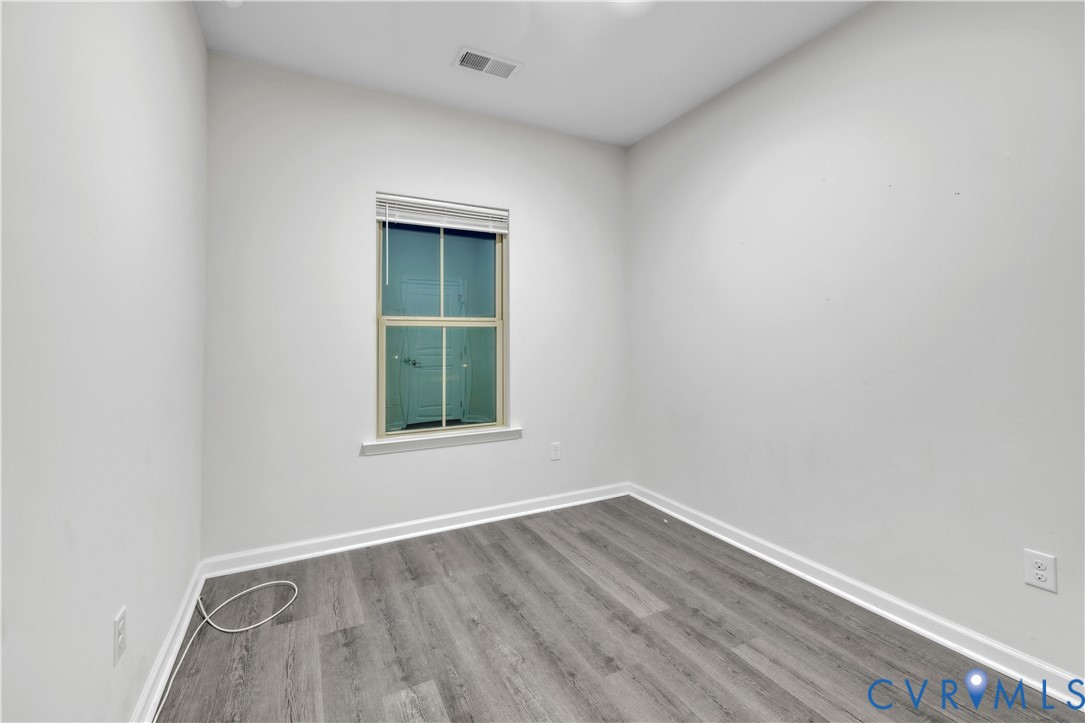 Interior space featuring wood-finish flooring, white walls, and a single-pane window with white horizontal blinds