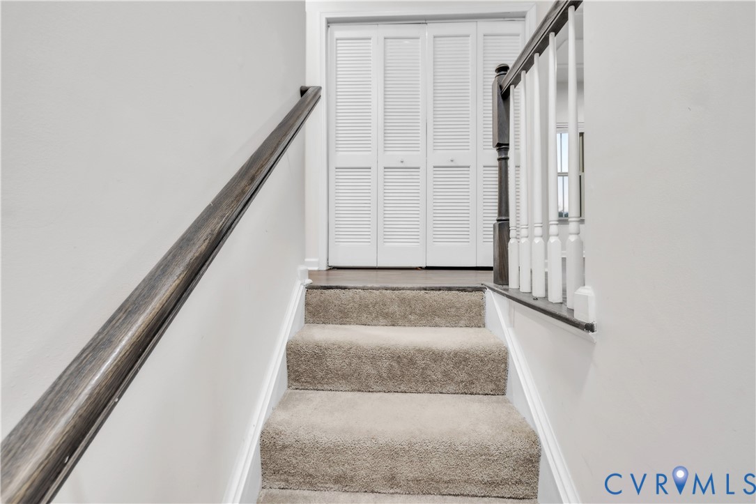 Staircase featuring wall-to-wall carpeting, dark-stained wood handrails, white wood balusters, and a four-panel louvered closet door