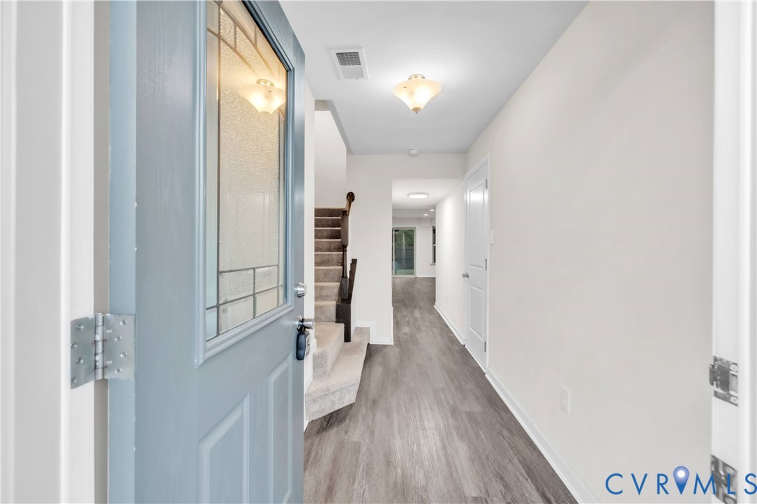 Entryway featuring a light blue front door with a textured glass panel, wood-finish flooring, and a staircase with dark wood-toned handrails Entryway featuring a light blue front door with a textured glass panel, wood-finish flooring, and a staircase with dark wood-toned handrails