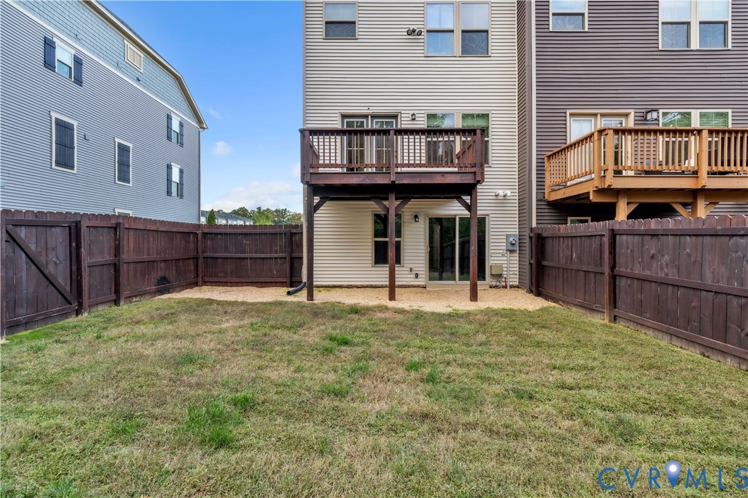 Rear exterior featuring a raised wood deck, ground-level stone patio, and perimeter wood privacy fencing