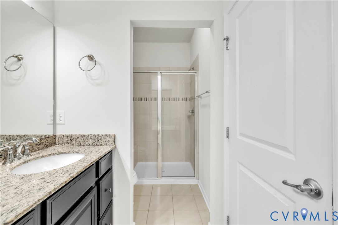 Bathroom featuring a vanity with stone-finish countertop, undermount sink, and dark cabinetry, paired with a glass-enclosed shower with tile surround and tile flooring