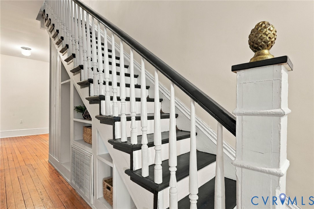 Staircase featuring white balusters, contrasting dark treads, a handrail, an ornate newel post cap, and built-in under-stair shelving
