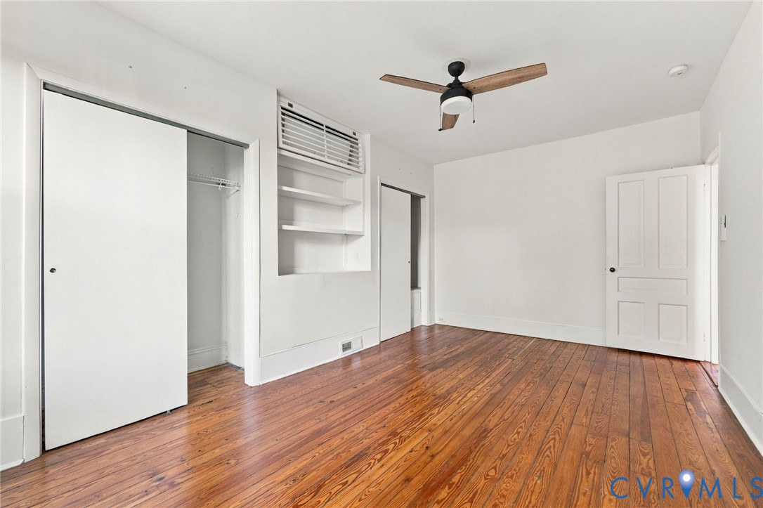 Front bedroom #2featuring wood-finish flooring, built-in shelving, a ceiling fan, a closet with sliding doors, and a multi-panel interior door