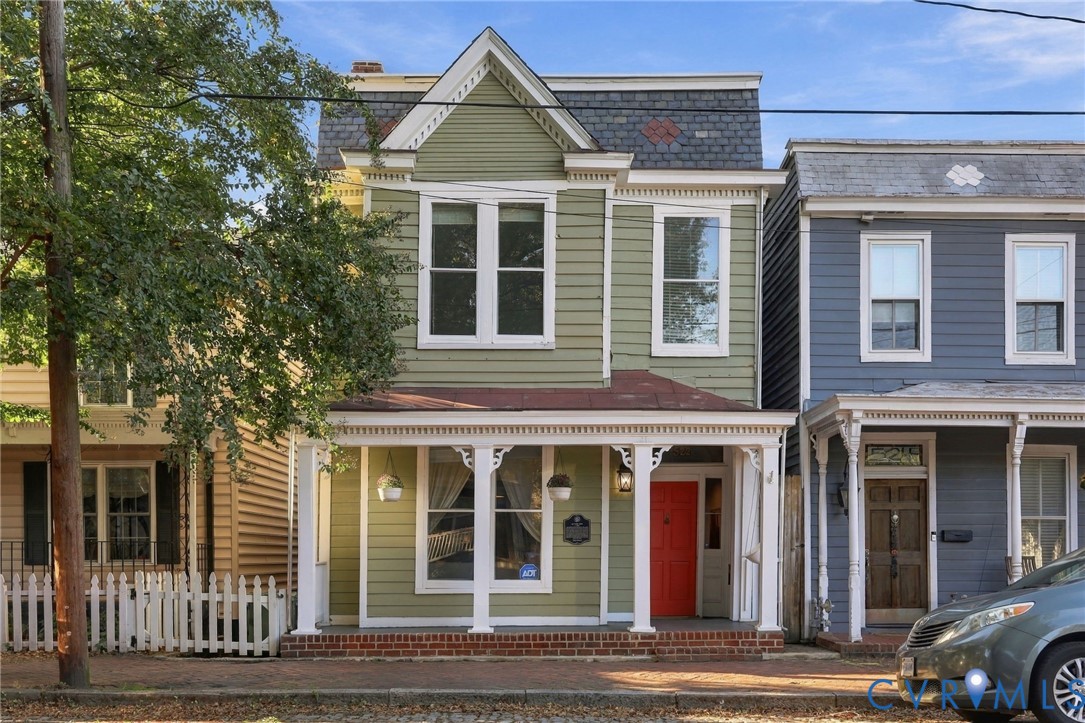 Two-story Victorian-style exterior featuring horizontal siding, a mansard roof with decorative shingle patterns, a covered front porch with ornate gingerbread trim, and a brick foundation