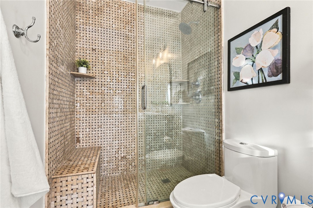 Walk-in shower featuring a built-in tiled bench, textured stone-style wall tile, glass enclosure with a sliding door, and an overhead rainfall showerhead