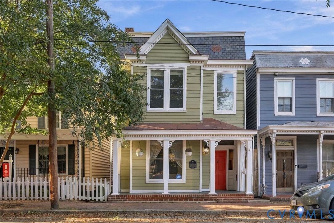 Two-story Victorian-style residence featuring horizontal lap siding, decorative roof shingles, a covered front porch with ornate millwork, and brick foundation detailing