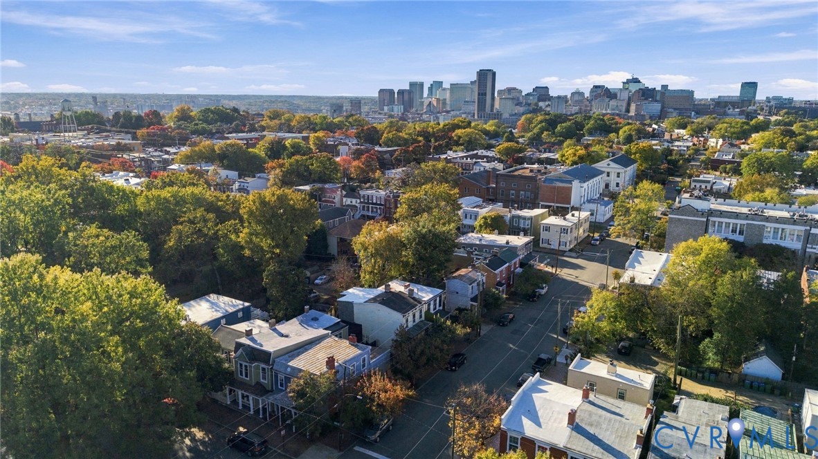 Aerial perspective featuring an established neighborhood with mature trees and a city skyline backdrop