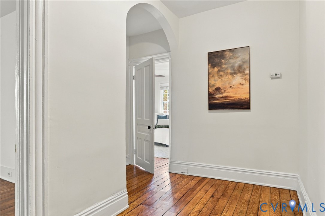 Architectural arched opening featuring natural wood-finish flooring and a classic five-panel interior door