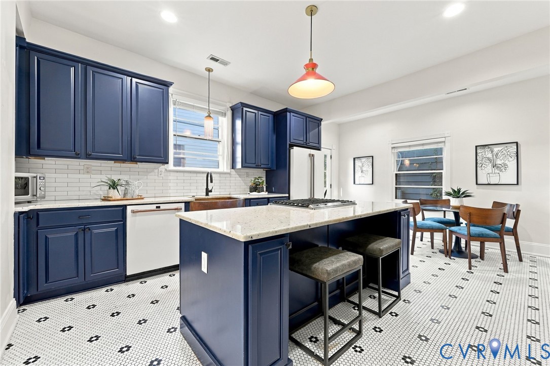 Kitchen featuring navy blue cabinetry, center island with stone-finish countertop, white subway tile backsplash, farmhouse-style sink, and geometric patterned floor tile