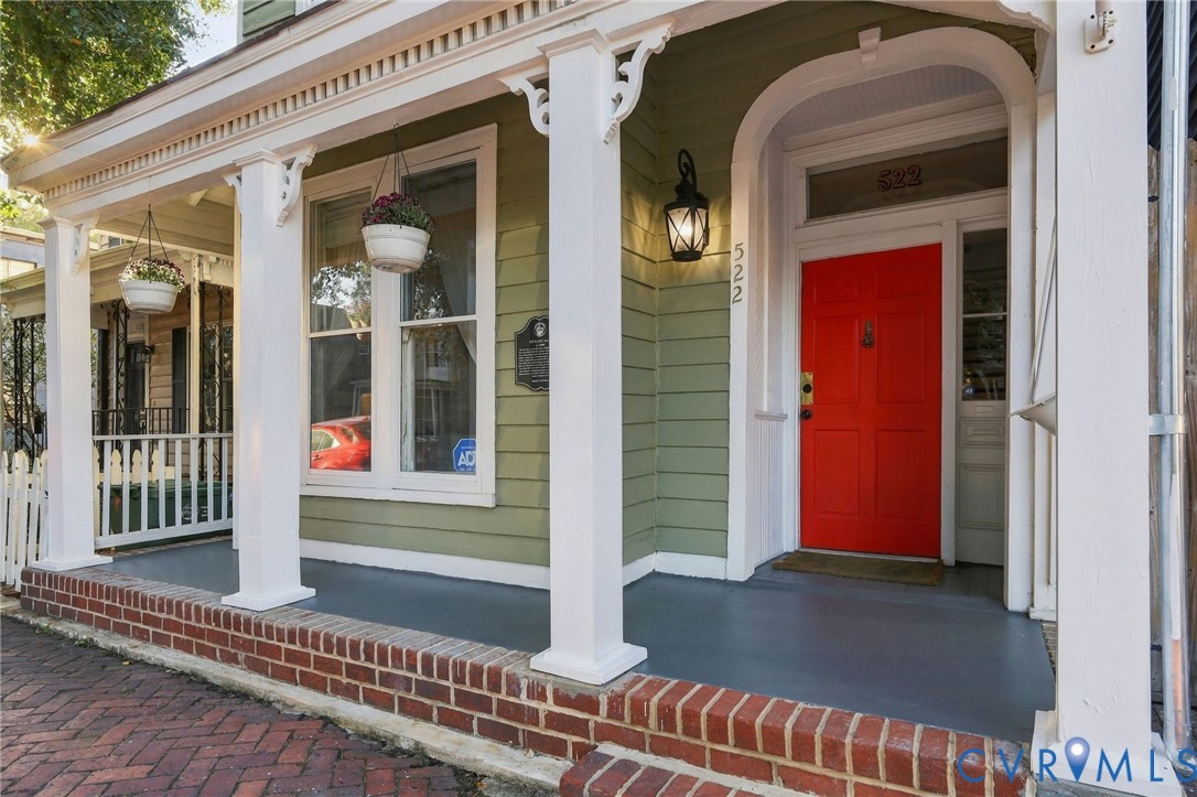 Covered front porch featuring decorative brackets, square columns, a transom window, and a brick-lined walkway