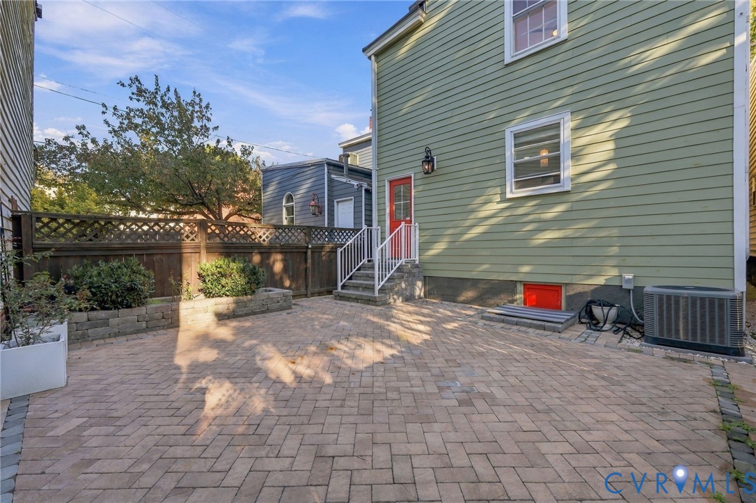 Rear exterior featuring a herringbone-pattern paver patio, wood lattice privacy fencing, stone retaining wall, and horizontal siding