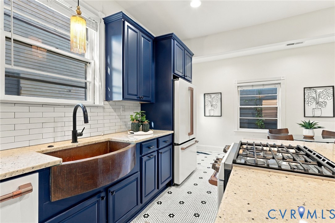 Kitchen featuring deep blue shaker-style cabinetry, copper farmhouse sink, stone-composite countertops, subway tile backsplash, and hexagonal mosaic floor tiling