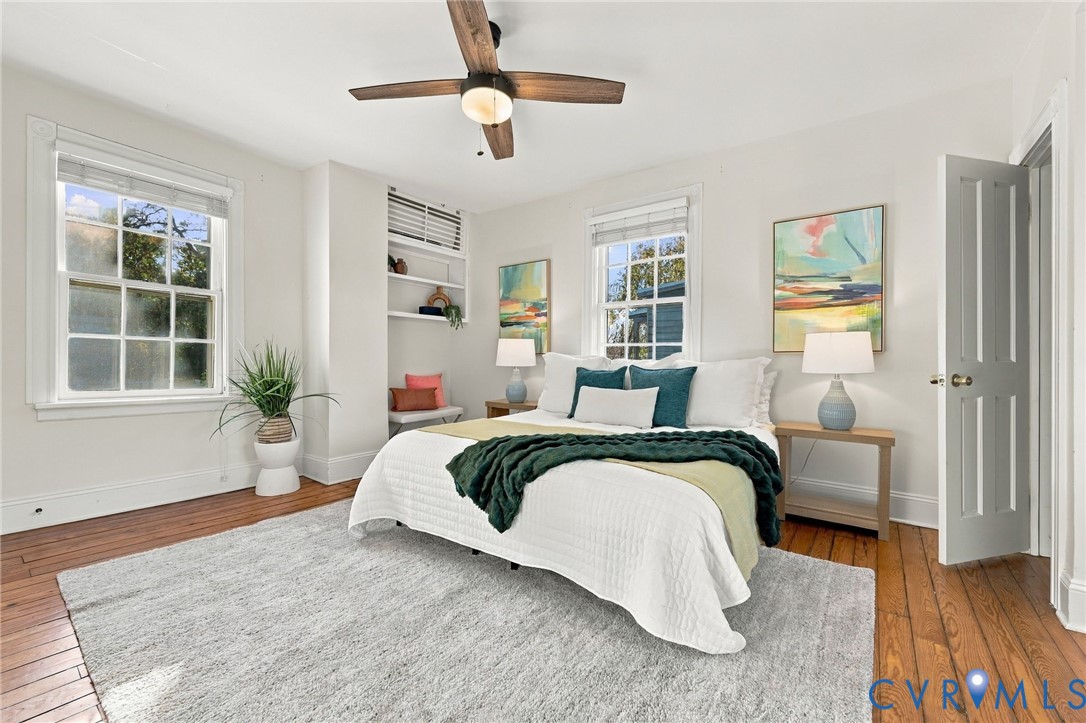 Room featuring wood-finish flooring, multi-pane windows, built-in shelving, and a ceiling fan with integrated lighting
