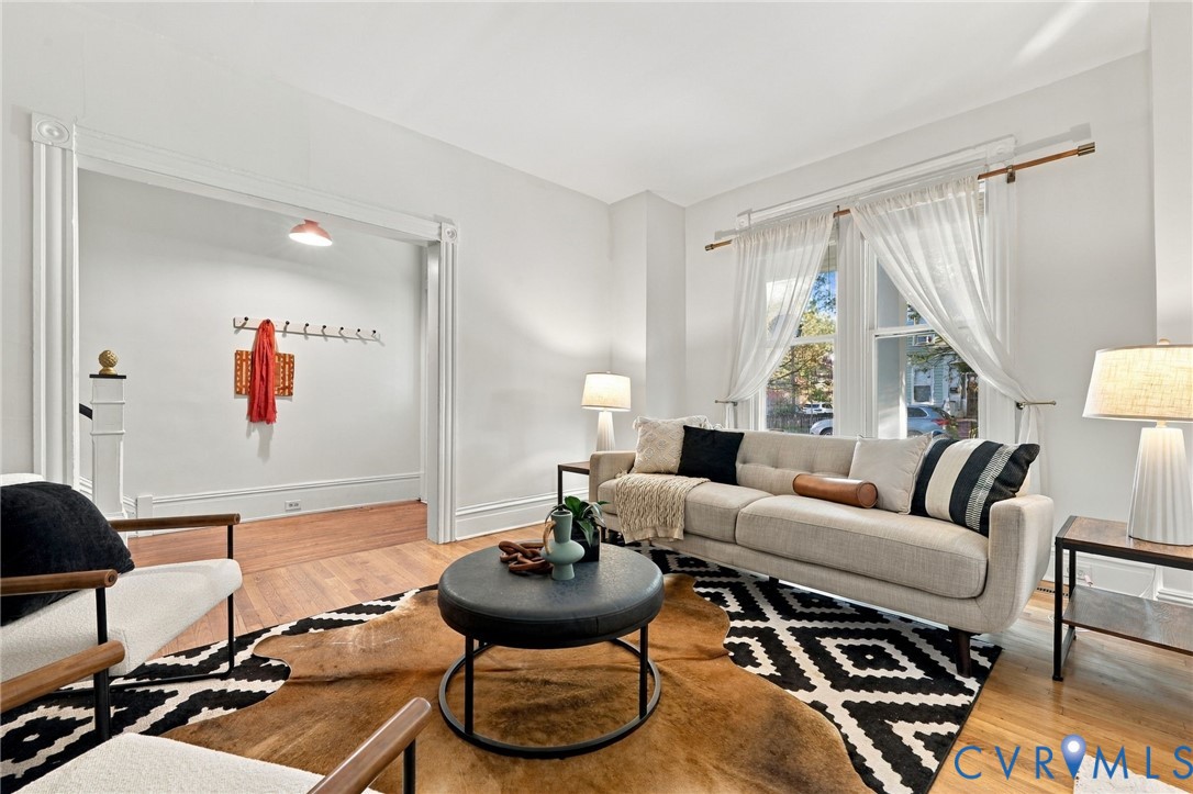 Living space featuring wood-finish flooring, extensive crown molding, wide doorway casings, and large windows with integrated hardware