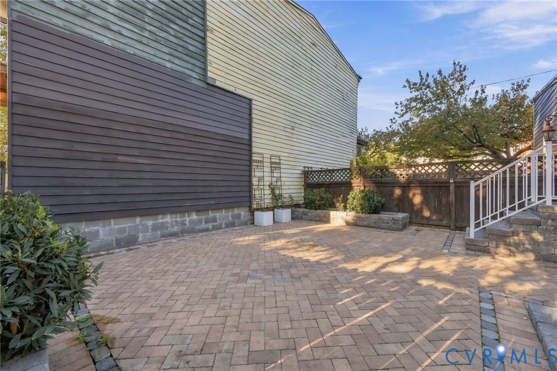 Herringbone-patterned paver patio featuring built-in stone planters, wood lattice-top fencing, and a white metal staircase