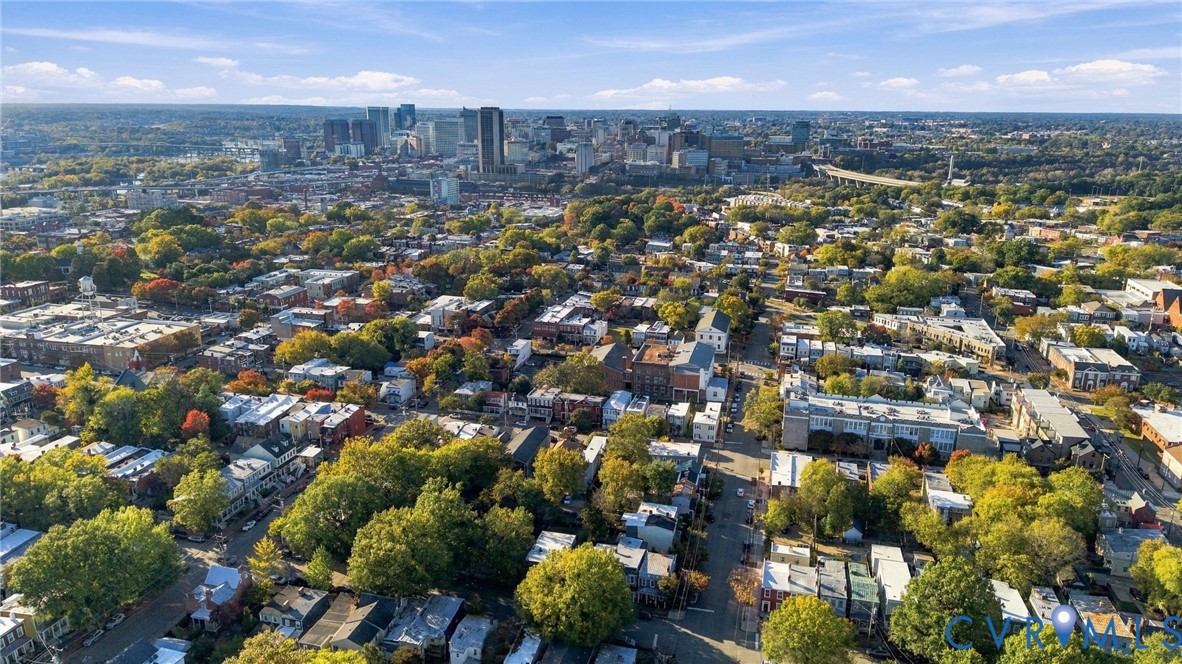 Aerial perspective featuring an expansive cityscape, mature tree canopy, and dense urban infrastructure