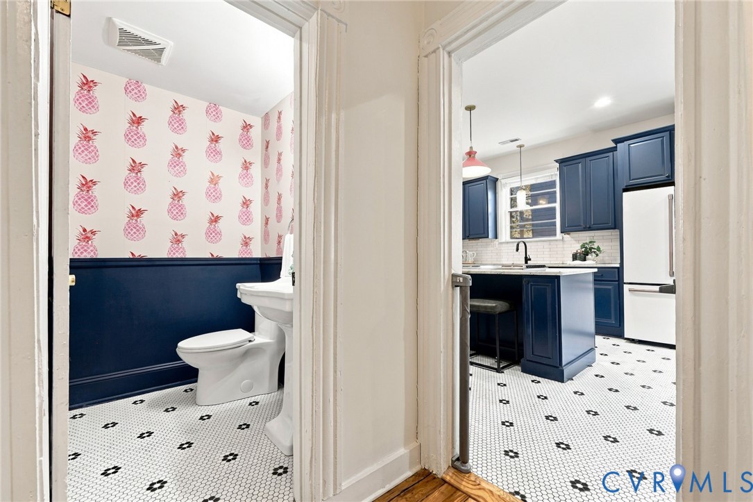 Half bath featuring a pedestal sink, patterned wallpaper, and navy wainscoting, with white and black hexagonal floor tile
