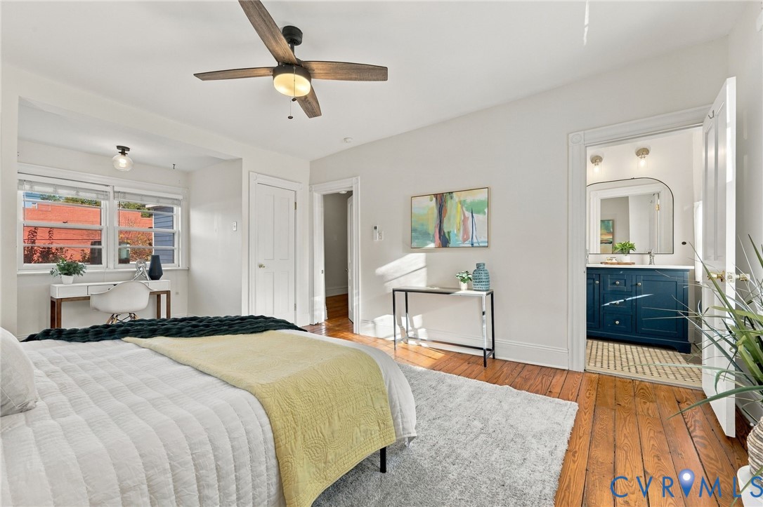 Hardwood flooring, ceiling fan with light fixture, multi-pane windows, and a bathroom featuring a navy blue vanity cabinet with a metallic faucet and arched mirror