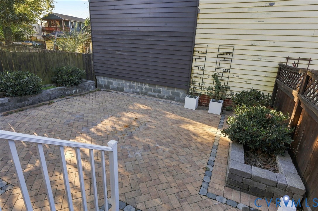 Herringbone-patterned paver patio featuring raised stone planters, a wood privacy fence, and metal decorative trellises
