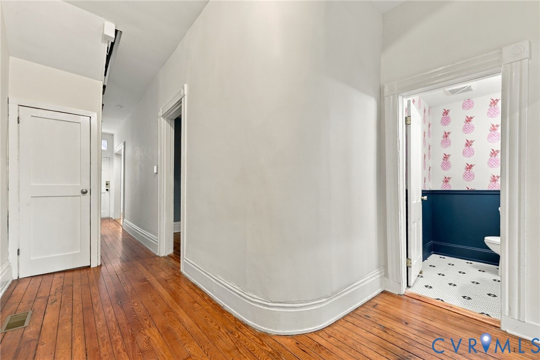 Hallway featuring wood-finish flooring, a curved architectural wall, and classic multi-panel interior doors with traditional millwork trim and view of the curved corner wall.
