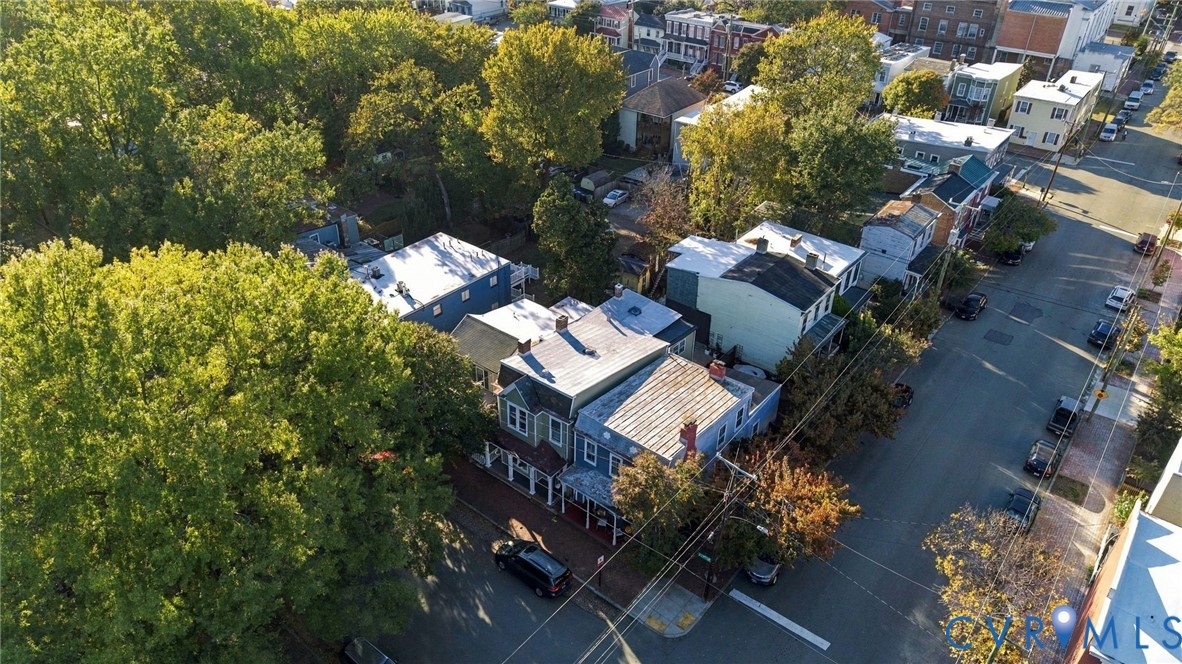Aerial view of multi-story residence featuring a covered front porch, metal roof, and brick exterior detailing, situated on a corner lot with established trees