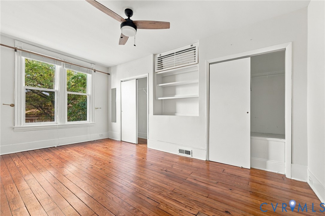 Front bedroom #2 featuring wood-finish flooring, a ceiling fan, built-in recessed shelving, dual-pane windows, and closet storage with sliding doors