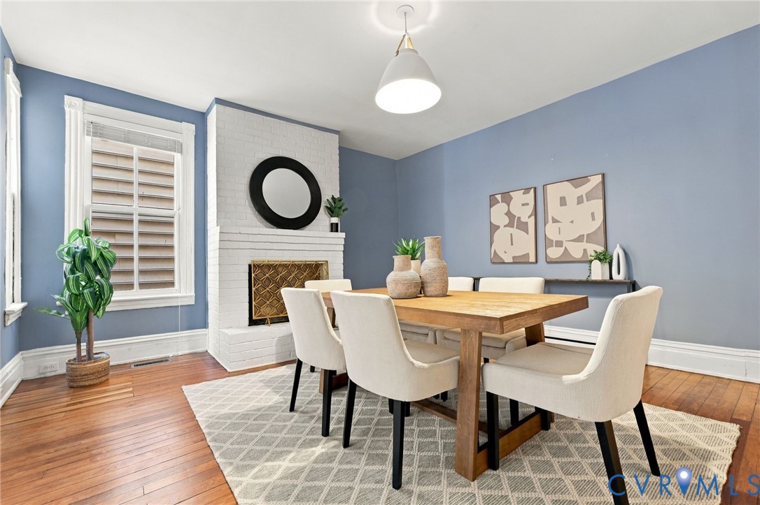 Painted brick fireplace with a metal fire screen, wood-finish flooring, and a pendant light fixture