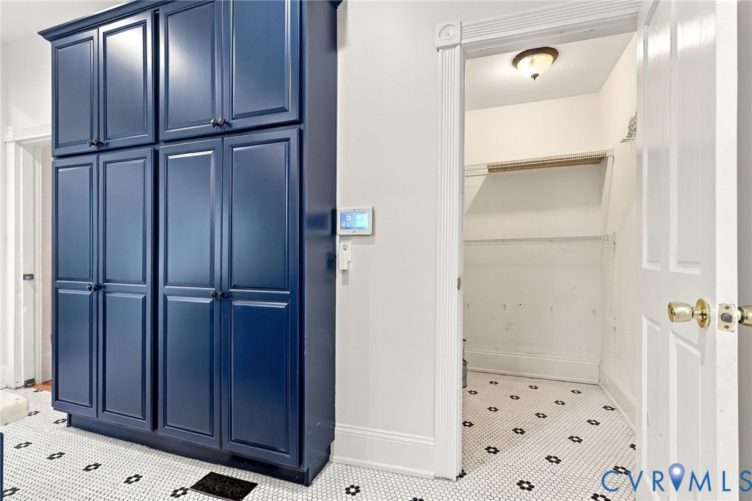 Floor-to-ceiling cabinetry with navy blue shaker-style doors, black circular hardware, geometric tile flooring, and integrated wall-mounted smart home control panel