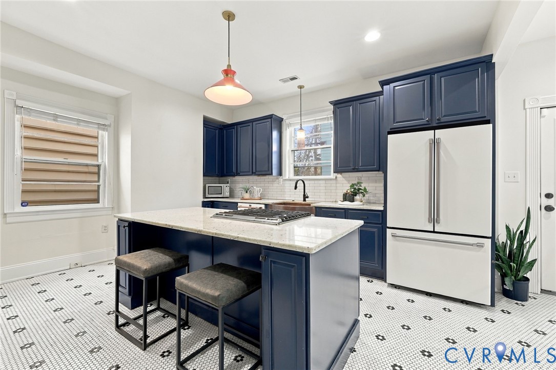 Kitchen featuring custom navy cabinetry, stone-surface island with an integrated gas cooktop, white subway tile backsplash, and decorative patterned floor tiling