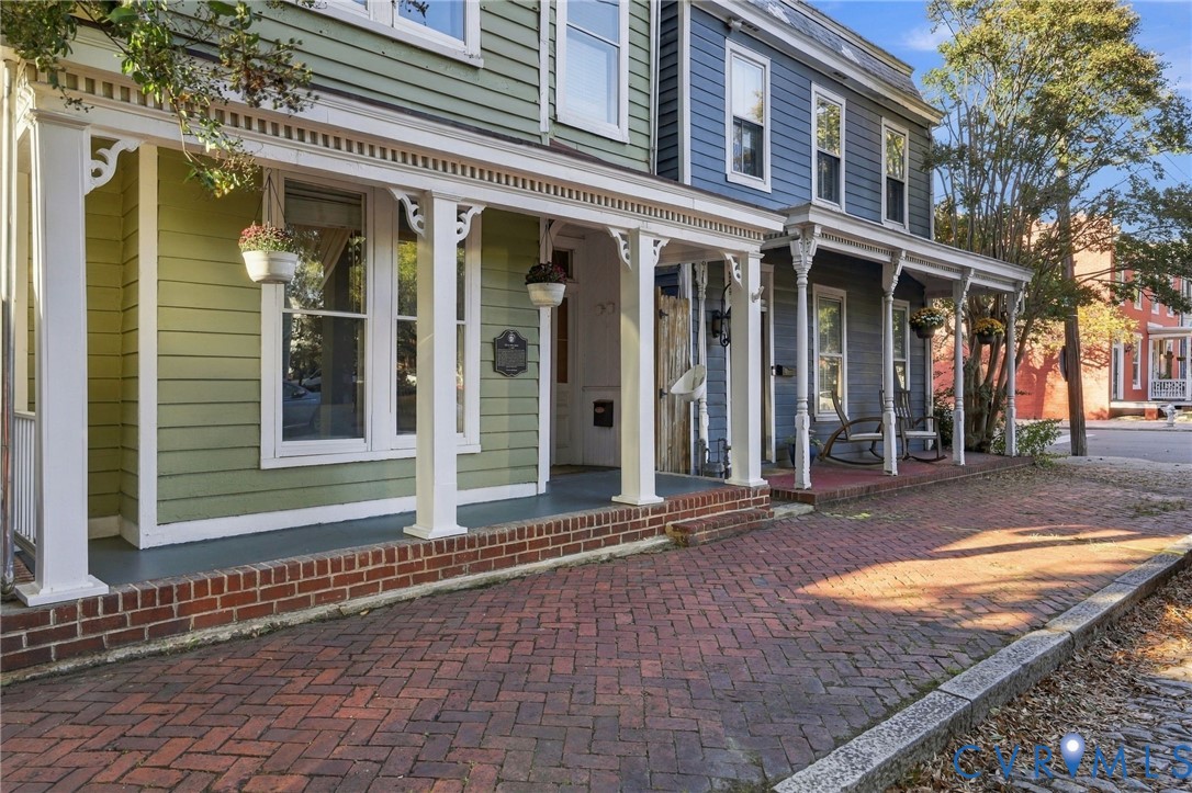 Historic exterior featuring multi-colored horizontal lap siding, covered wrap-around porch, ornamental wood brackets, and brick paved walkway