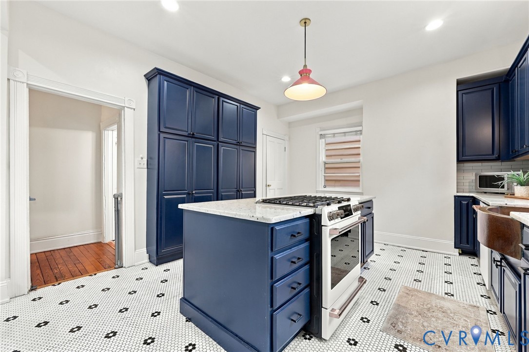 Kitchen featuring floor-to-ceiling blue cabinetry, a central island with a gas range and stone countertop, a copper apron-front sink, and patterned tile flooring