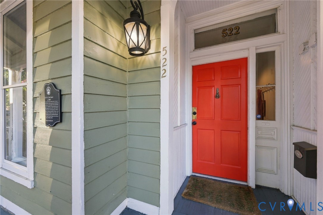 Exterior entry featuring horizontal lap siding, a paneled door with glass transom, sidelight with built-in mail slot, and an attached decorative wall-mounted lantern