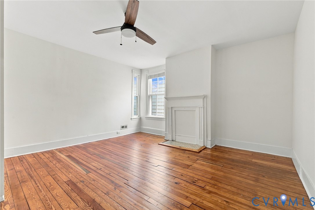 Bedroom #3 featuring wood-finish flooring, a white-mantel fireplace with a mosaic-tiled hearth, and a modern three-blade ceiling fan