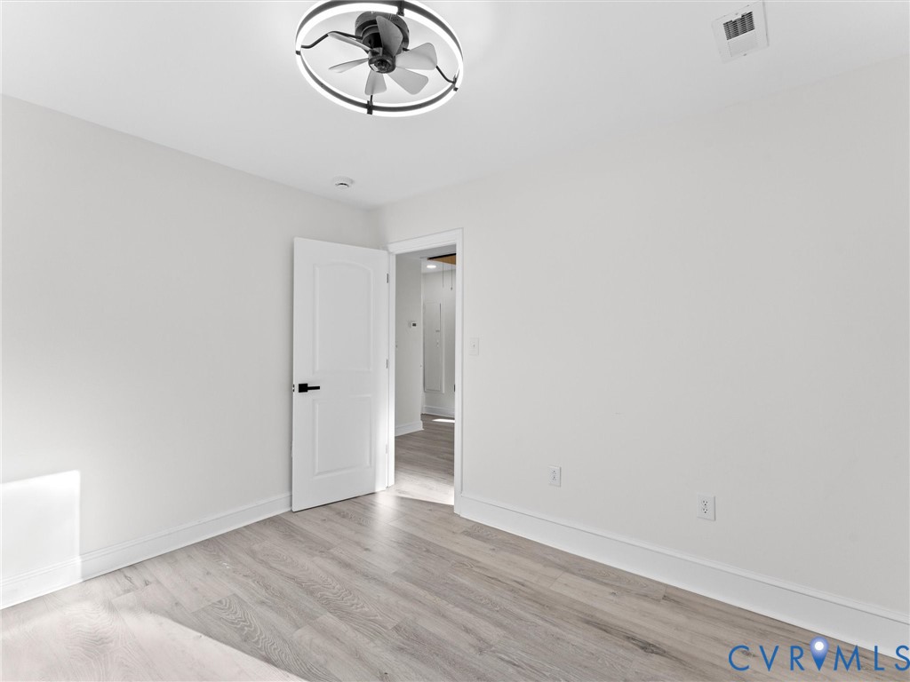 Interior room featuring wood-finish flooring, a modern circular LED ceiling fan, and a single-panel interior door with matte black hardware