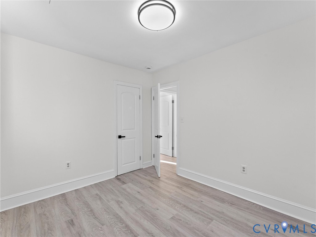 Wood-finish flooring, two-panel interior doors, matte black lever hardware, and a modern circular flush-mount ceiling light fixture