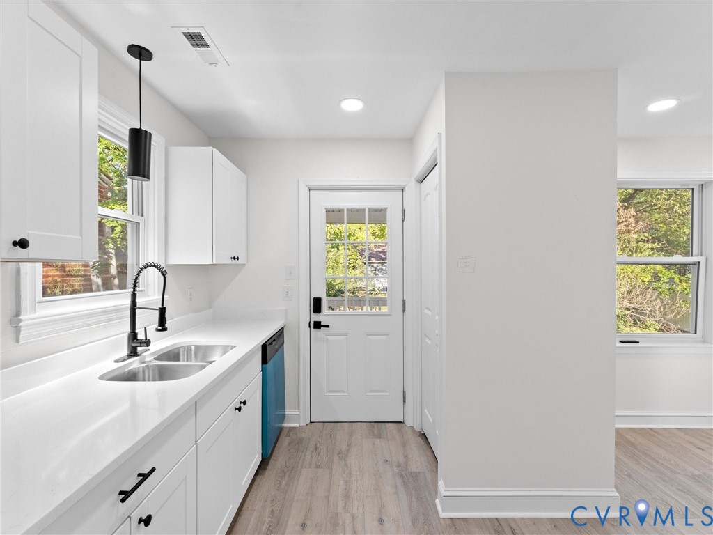 Kitchen area featuring white shaker-style cabinetry, solid-surface countertops, dual-basin stainless steel sink with a matte black faucet, and wood-finish flooring