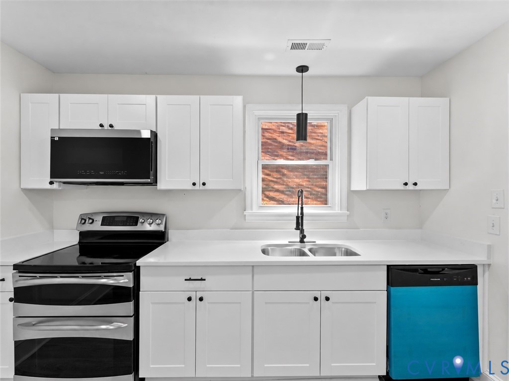 Kitchen featuring white cabinetry, quartz countertops, dual-basin stainless steel sink with matte black faucet, and stainless steel appliances