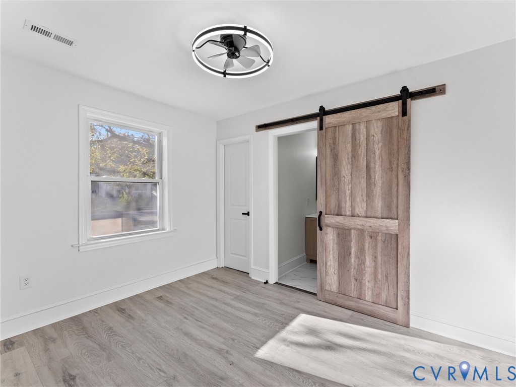 Interior space featuring wood-finish flooring, a sliding barn door with matte black hardware, and a modern circular ceiling fan with integrated lighting