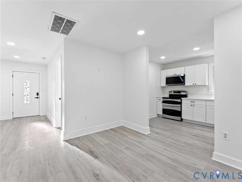 Kitchen featuring white shaker-style cabinetry, stainless steel appliances, and solid surface countertops, finished with wood-finish flooring and recessed lighting