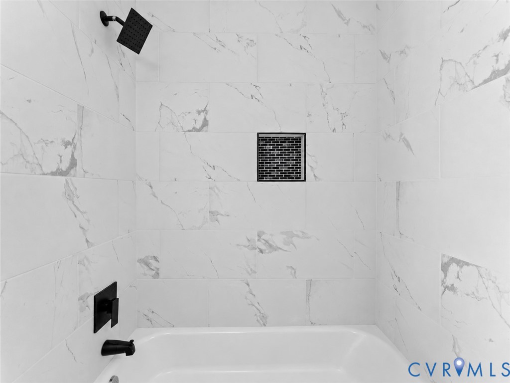 Shower enclosure featuring large-format tile with veining, matte black rainfall showerhead, matching wall-mounted faucet and tub spout, and a built-in recessed tile niche
