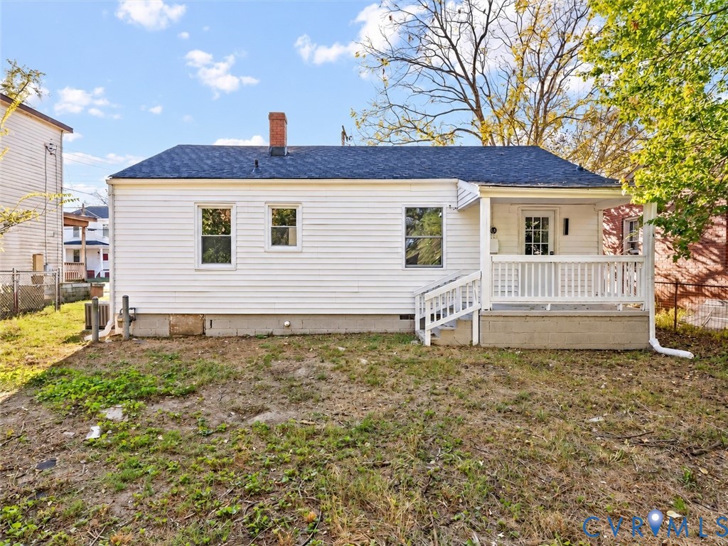 Single-story exterior featuring white vinyl siding, a gabled roof with asphalt shingles, a brick chimney, and a covered front porch with a white railing
