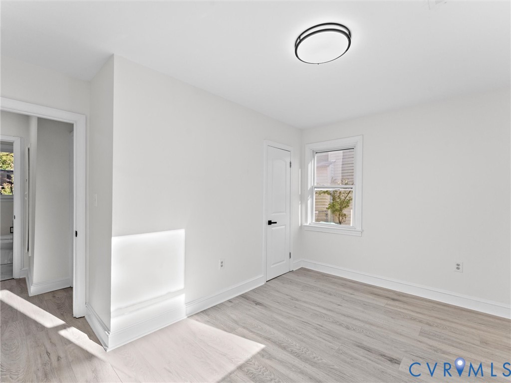 Interior room featuring wood-finish flooring, a neutral color palette, a single-hung window, a modern circular flush-mount ceiling light, and a six-panel door with matte black hardware