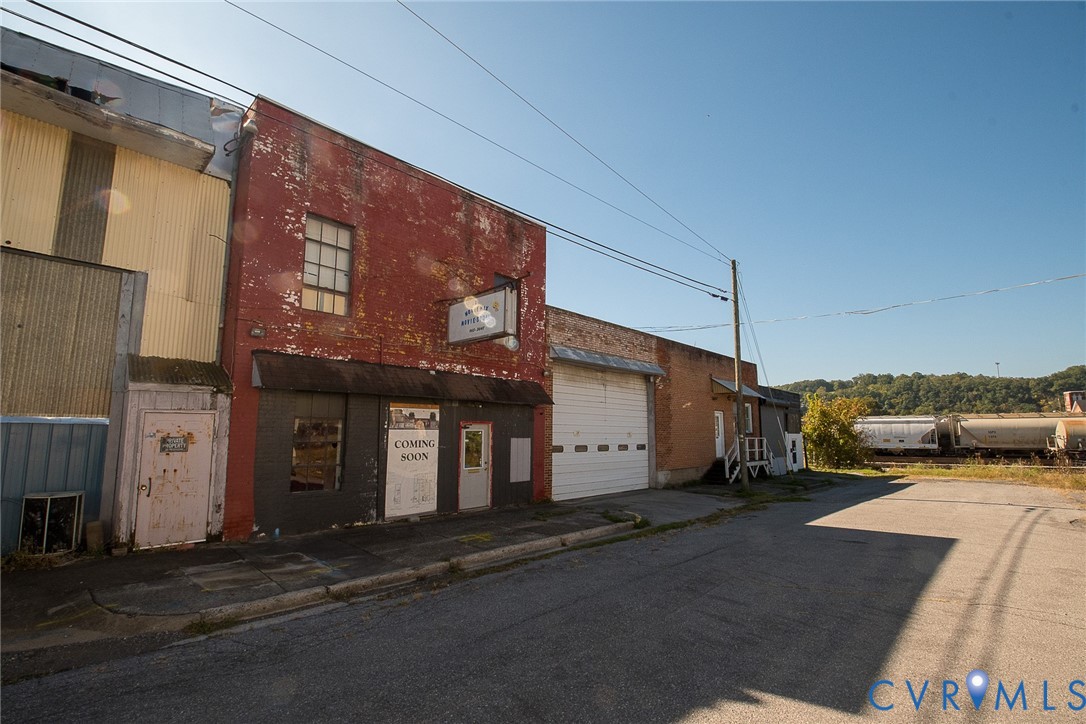 Multi-story red brick masonry facade featuring large metal roll-up warehouse door, storefront entrance, and corrugated metal siding accents